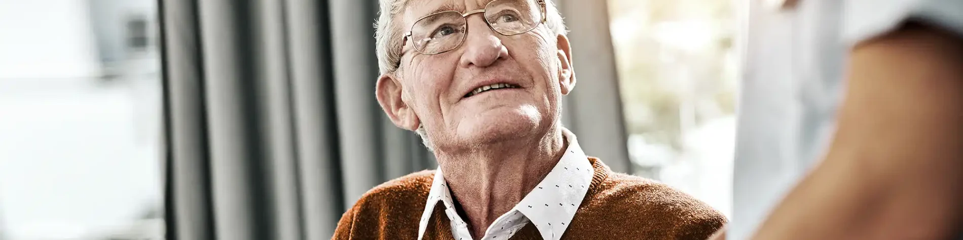 Ein älterer Mann blickt zur Pflegekraft auf und sie hält seine Hand. | VIACTIV Krankenkasse