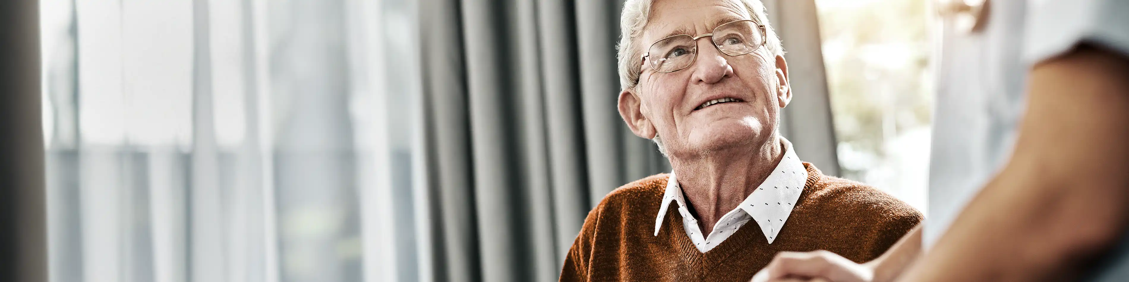 Ein älterer Mann blickt zur Pflegekraft auf und sie hält seine Hand. | VIACTIV Krankenkasse