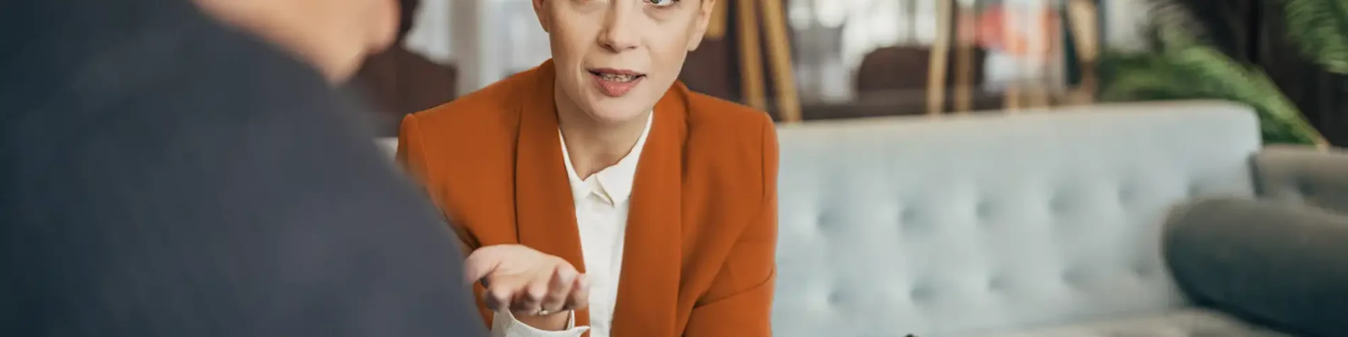 Eine Frau sitzt auf dem Sofa. Ihr gegenüber sitzt ein älterer Mann, mit dem sie sich unterhält. | VIACTIV Krankenkasse