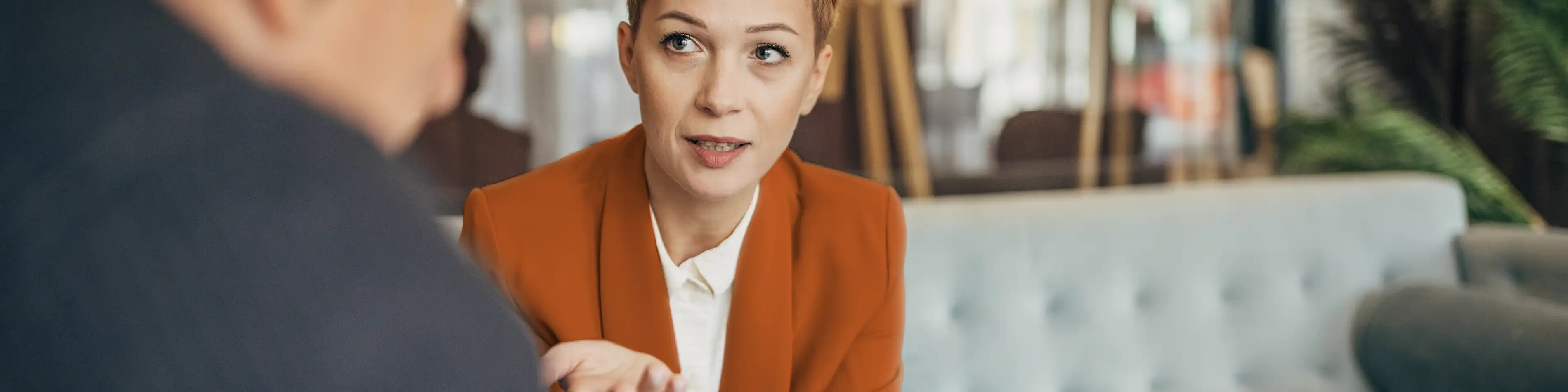 Eine Frau sitzt auf dem Sofa. Ihr gegenüber sitzt ein älterer Mann, mit dem sie sich unterhält. | VIACTIV Krankenkasse