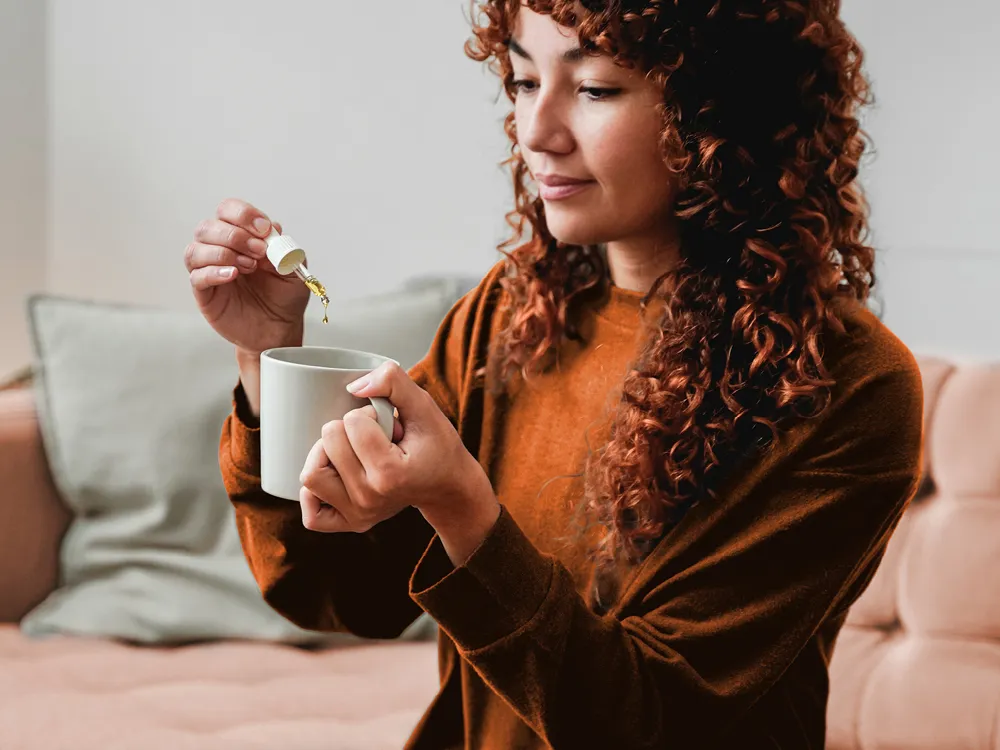 Eine junge Frau tropft sich pflanzliche Arzneimittel in ihr Getränk. | VIACTIV Krankenkasse