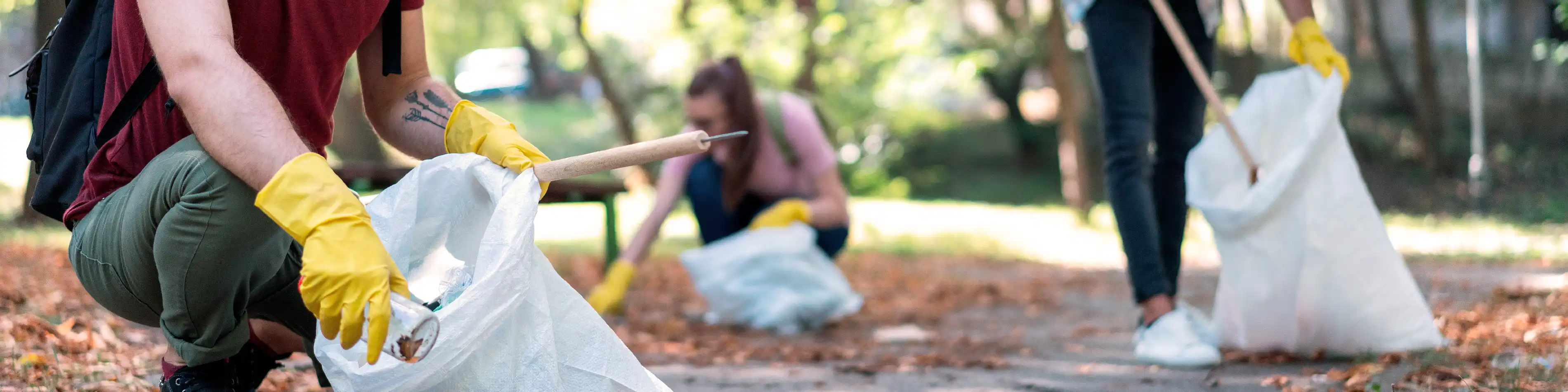 Mehrere Personen sammeln mit Handschuhen in einem Park Müll ein und beteiligen sich an der Plogging Challenge. | VIACTIV Krankenkasse