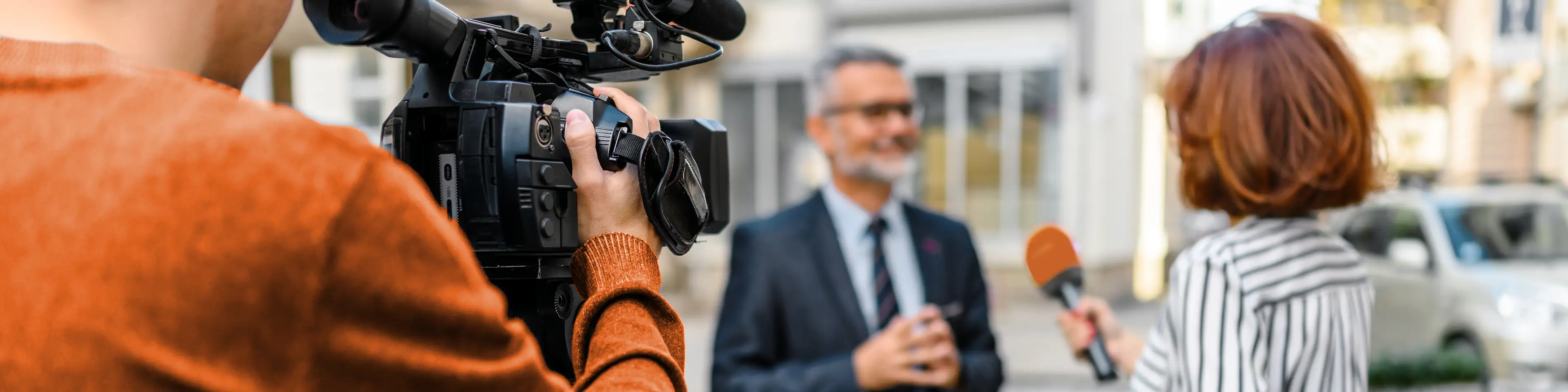 Eine Reporterin interviewt einen Mann im Anzug. Sie hält ein Mikrofon in der Hand. Ein Kameramann filmt das Gespräch. | VIACTIV Krankenkasse