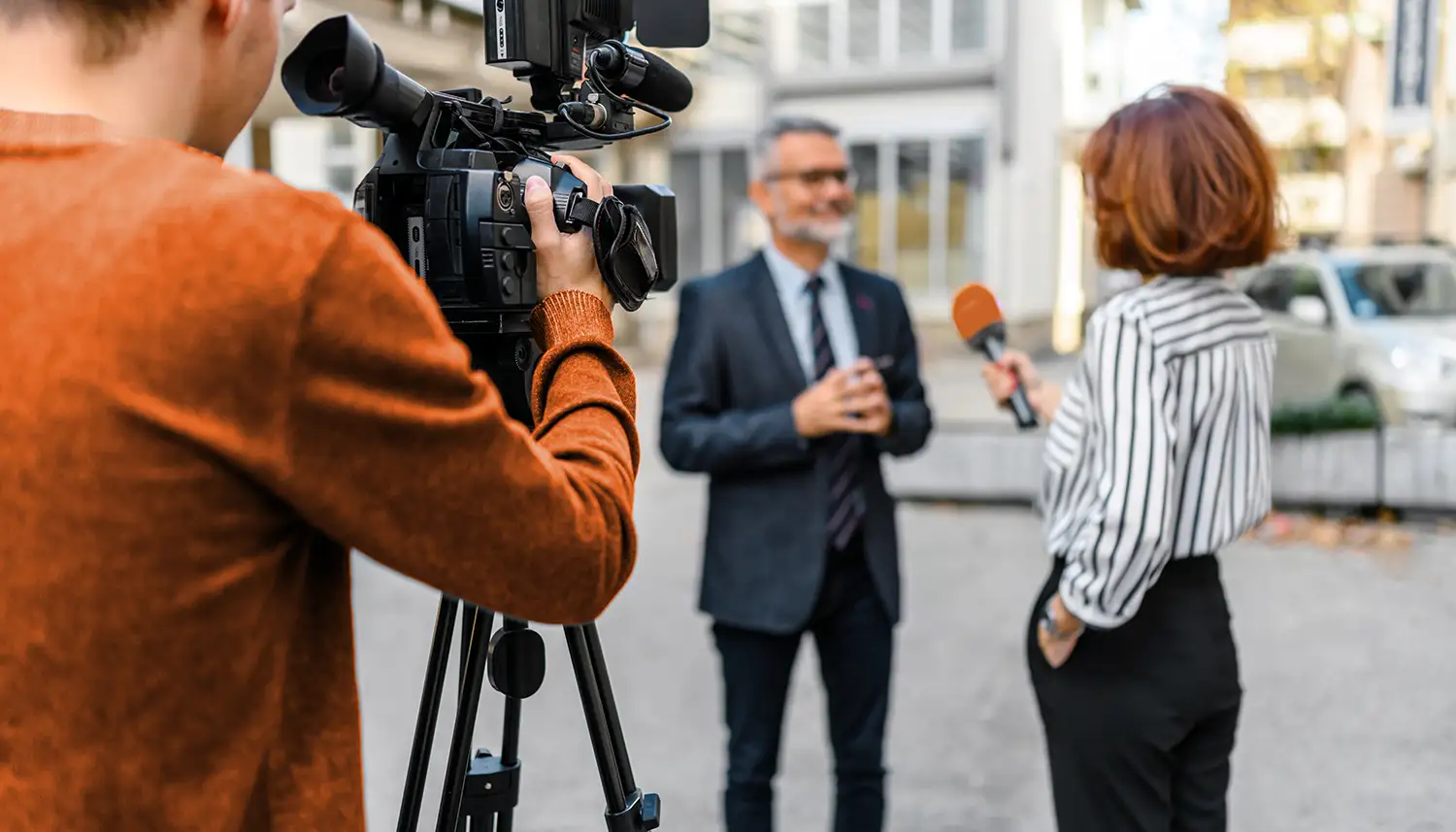 Eine Reporterin interviewt einen Mann im Anzug. Sie hält ein Mikrofon in der Hand. Ein Kameramann filmt das Gespräch. | VIACTIV Krankenkasse