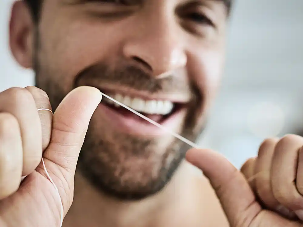 Ein Mann hält einen Faden Zahnseide gespannt zwischen den Händen und lacht in die Kamera. | VIACTIV Krankenkasse