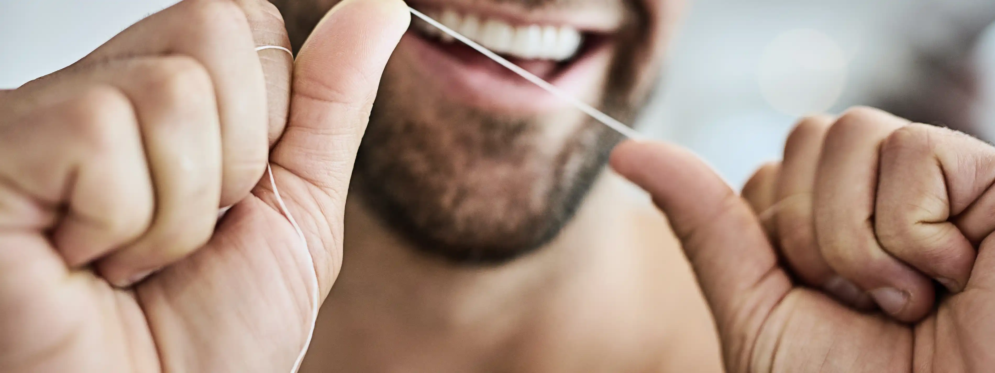 Ein Mann hält einen Faden Zahnseide gespannt zwischen den Händen und lacht in die Kamera. | VIACTIV Krankenkasse