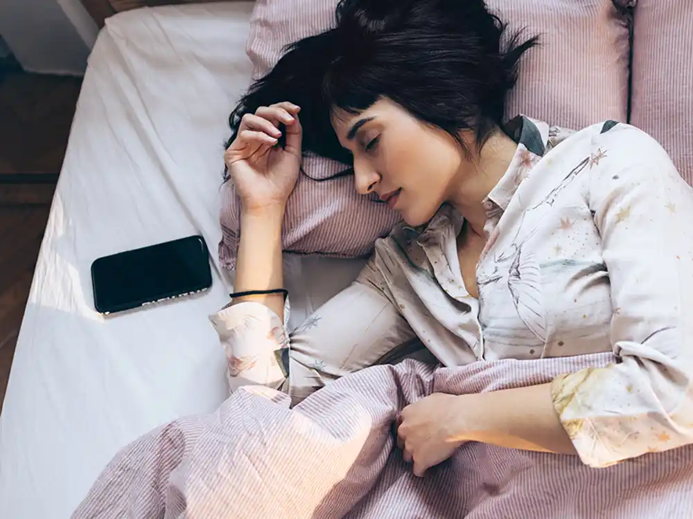 Auf dem Bild ist eine junge Frau beim Schlafen zu sehen. Neben ihr liegt ein Smartphone. | VIACTIV Krankenkasse
