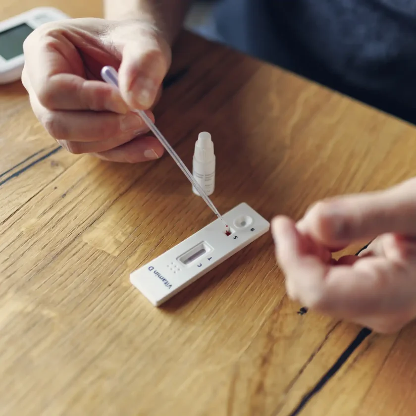 Auf einem Tisch liegt ein kleiner Vitamin D Test. Eine Person, dessen Hände man nur sieht, tropft eine Probe auf den Test. | VIACTIV Krankenkasse