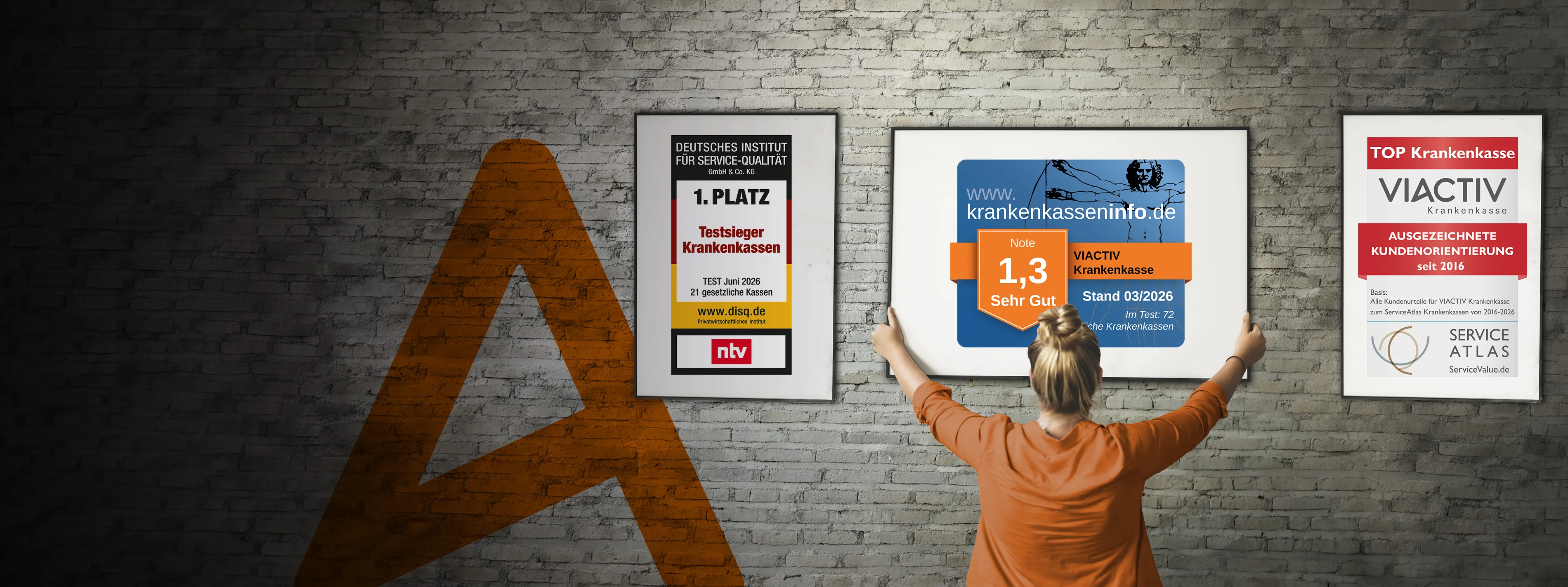 Eine Frau hängt Bilderrahmen an einer Wand auf. In den Bilderrahmen sind die aktuellen Auszeichnungen der VIACTIV Krankenkasse. | VIACTIV Krankenkasse