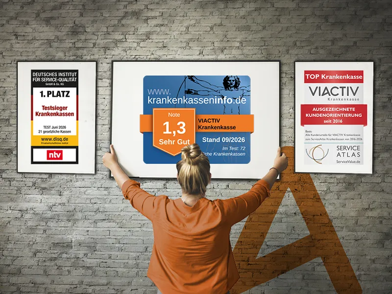 Eine Frau hängt Bilderrahmen an einer Wand auf. In den Bilderrahmen sind die aktuellen Auszeichnungen der VIACTIV Krankenkasse. | VIACTIV Krankenkasse