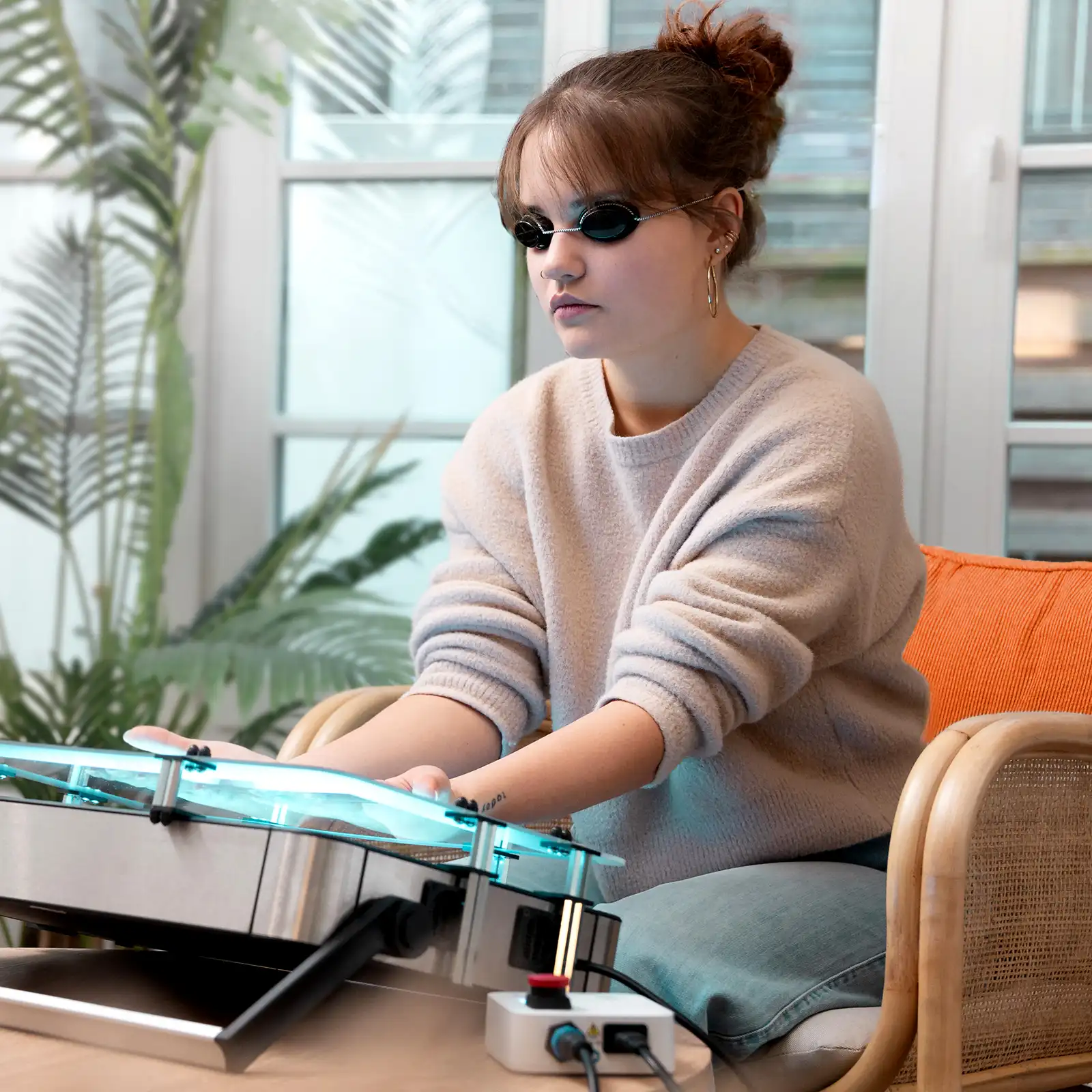 Eine junge Frau sitzt zuhause und macht eine Lichttherapie an ihren Händen. | VIACTIV Krankenkasse