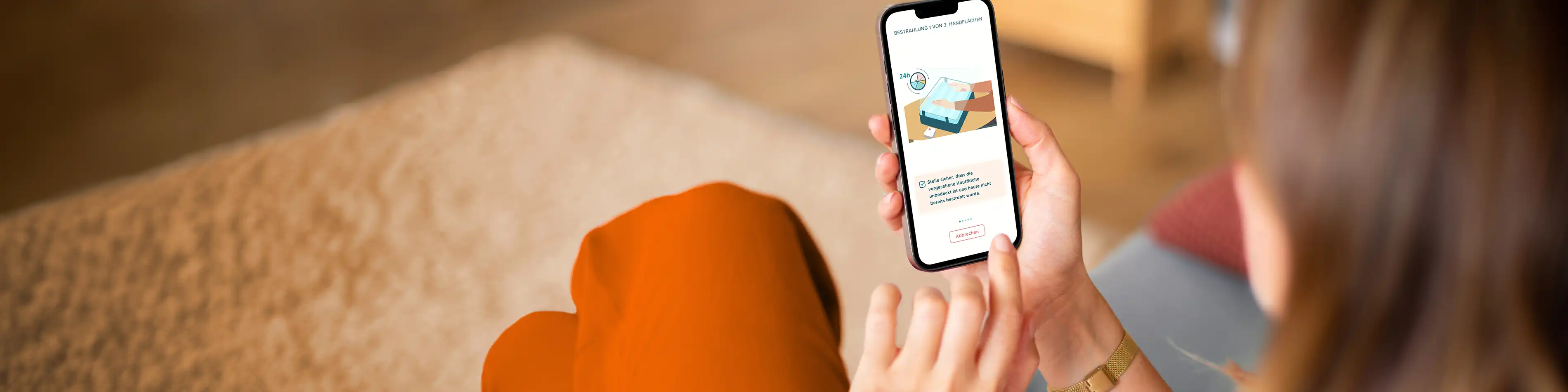 Eine Frau sitzt auf einem Sofa und schaut sich über ihr Smartphone die App Skinuvita an. | VIACTIV Krankenkasse