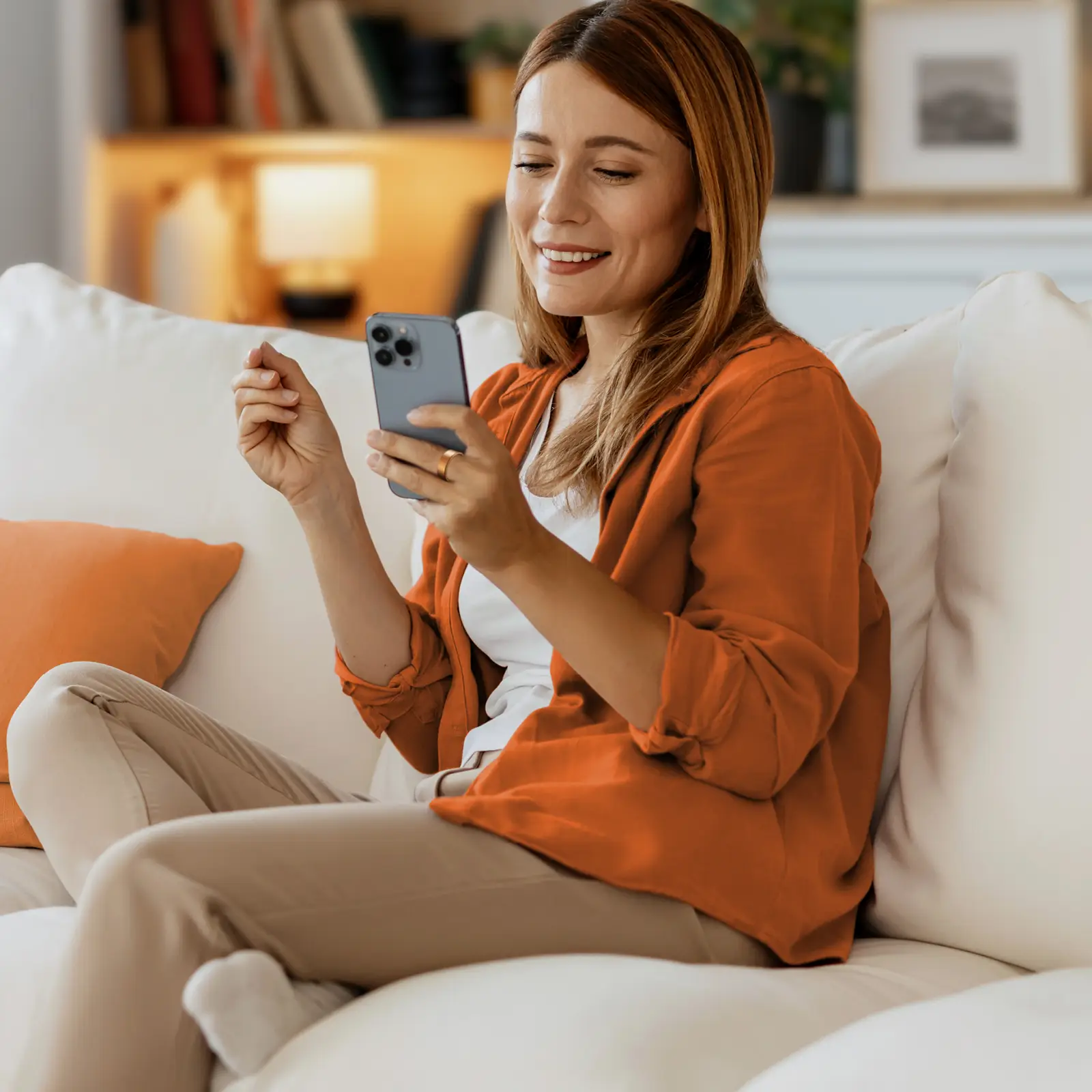 Eine junge Frau sitzt auf dem Sofa und schaut auf ihr Smartphone. Sie trägt einen Smartring. | VIACTIV Krankenkasse