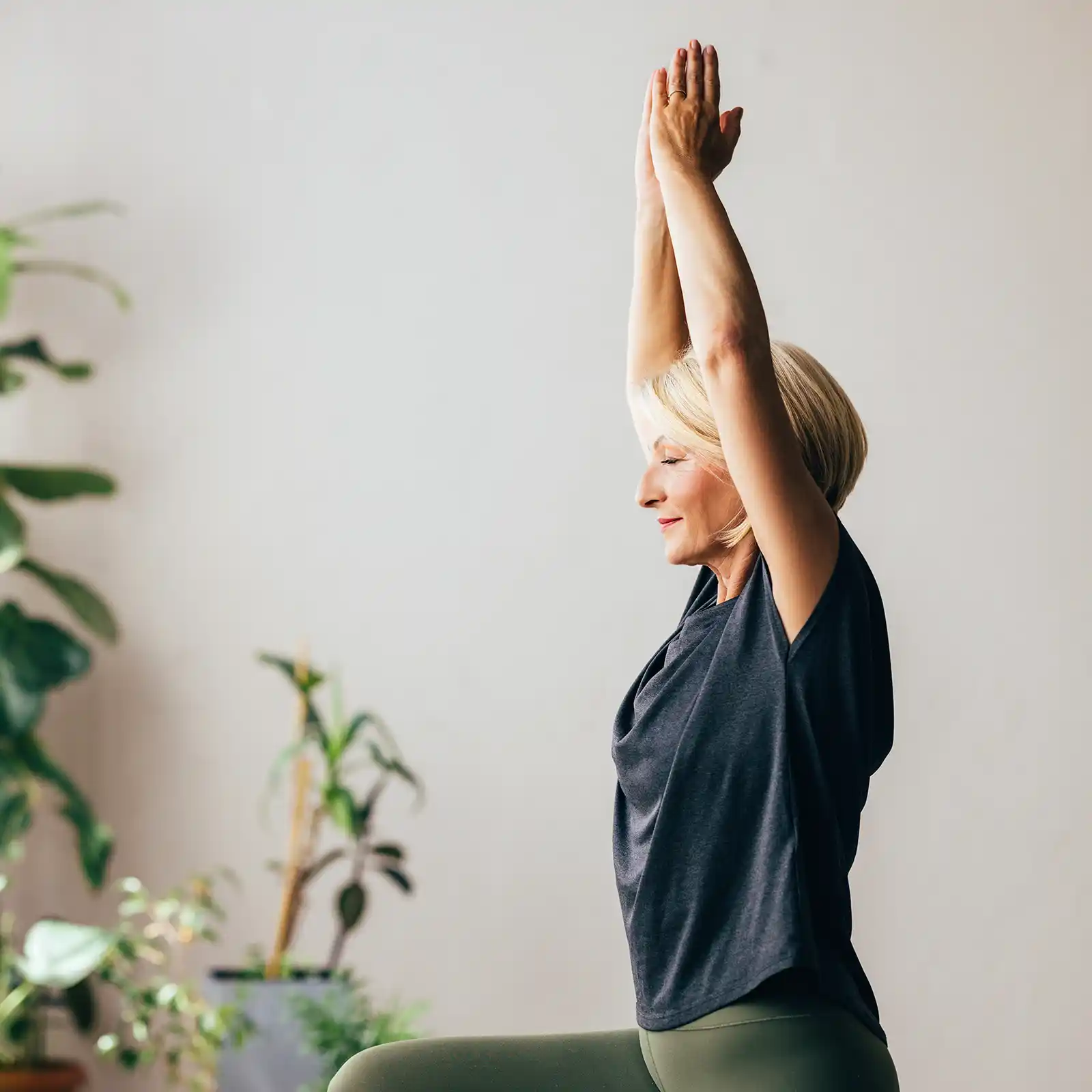 Eine Frau macht eine Yoga-Übung. Sie streckt beide Arme in die Höhe. Ihre Hände berühren sich über dem Kopf. Ihr Gesicht ist entspannt. | VIACTIV Krankenkasse