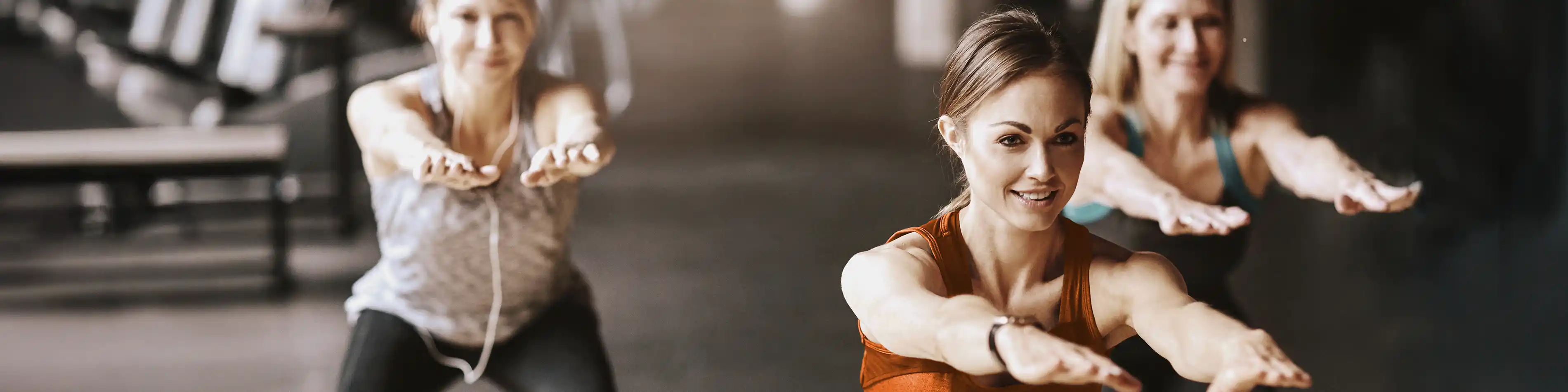 Eine Gruppe von jungen Frauen trainiert im Fitnessstudio und sie machen Kniebeugen. | VIACTIV Krankenkasse