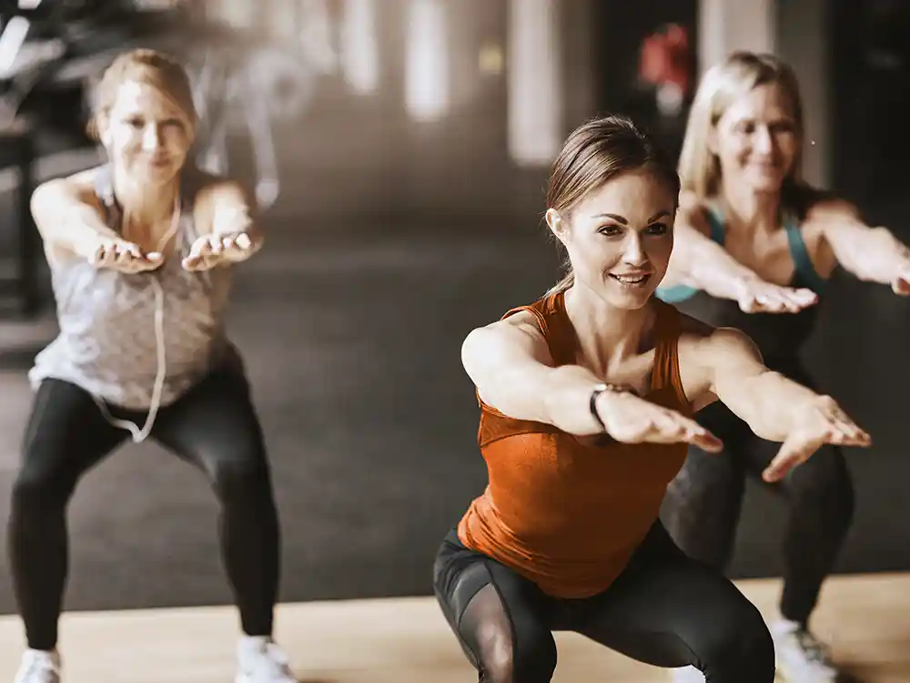 Eine Gruppe von jungen Frauen trainiert im Fitnessstudio und sie machen Kniebeugen. | VIACTIV Krankenkasse