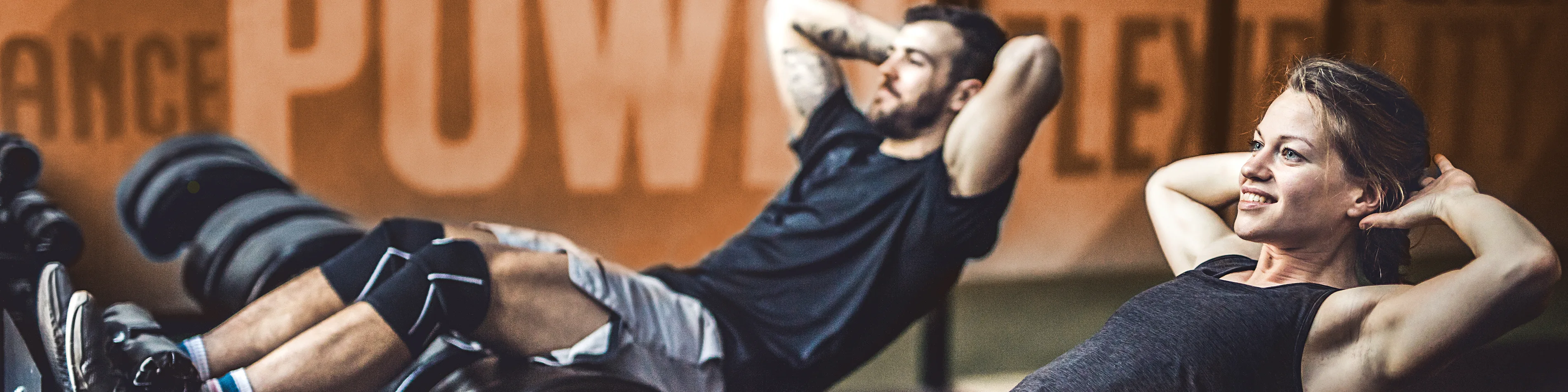 Eine Frau und ein Mann sind im Fitnessstudio und machen dort Sit-ups. | VIACTIV Krankenkasse