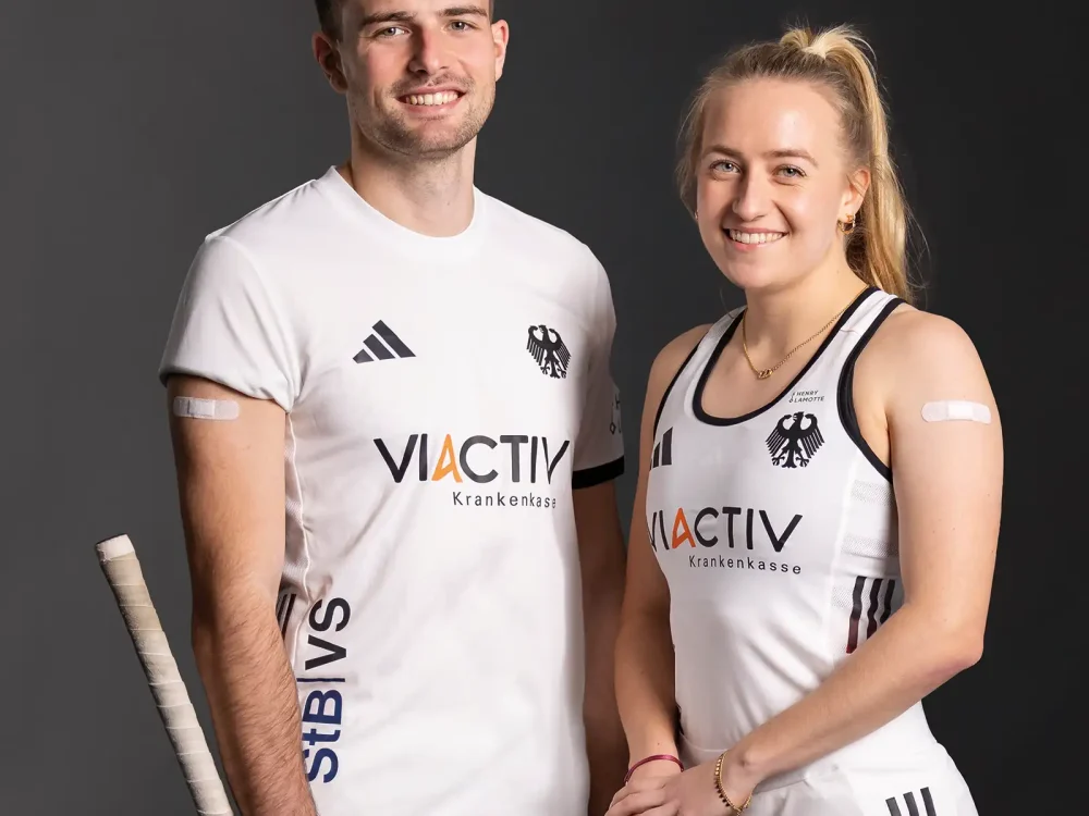 Ein Spieler und eine Spielerin vom Deutschen Hockey Bund stehen nebeneinander. Beide haben ein Pflaster auf dem Arm. | VIACTIV Krankenkasse