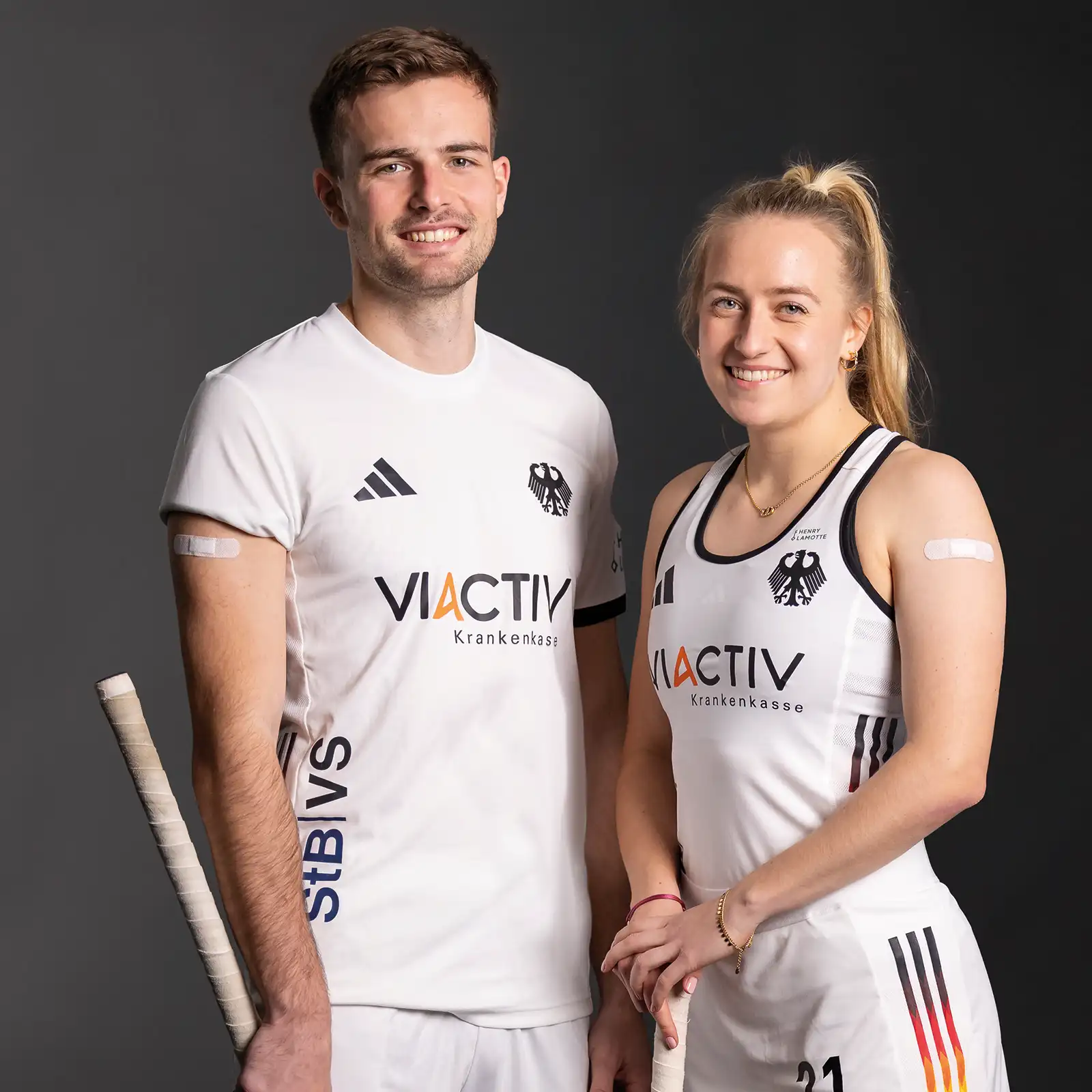 Ein Spieler und eine Spielerin vom Deutschen Hockey Bund stehen nebeneinander. Beide haben ein Pflaster auf dem Arm. | VIACTIV Krankenkasse