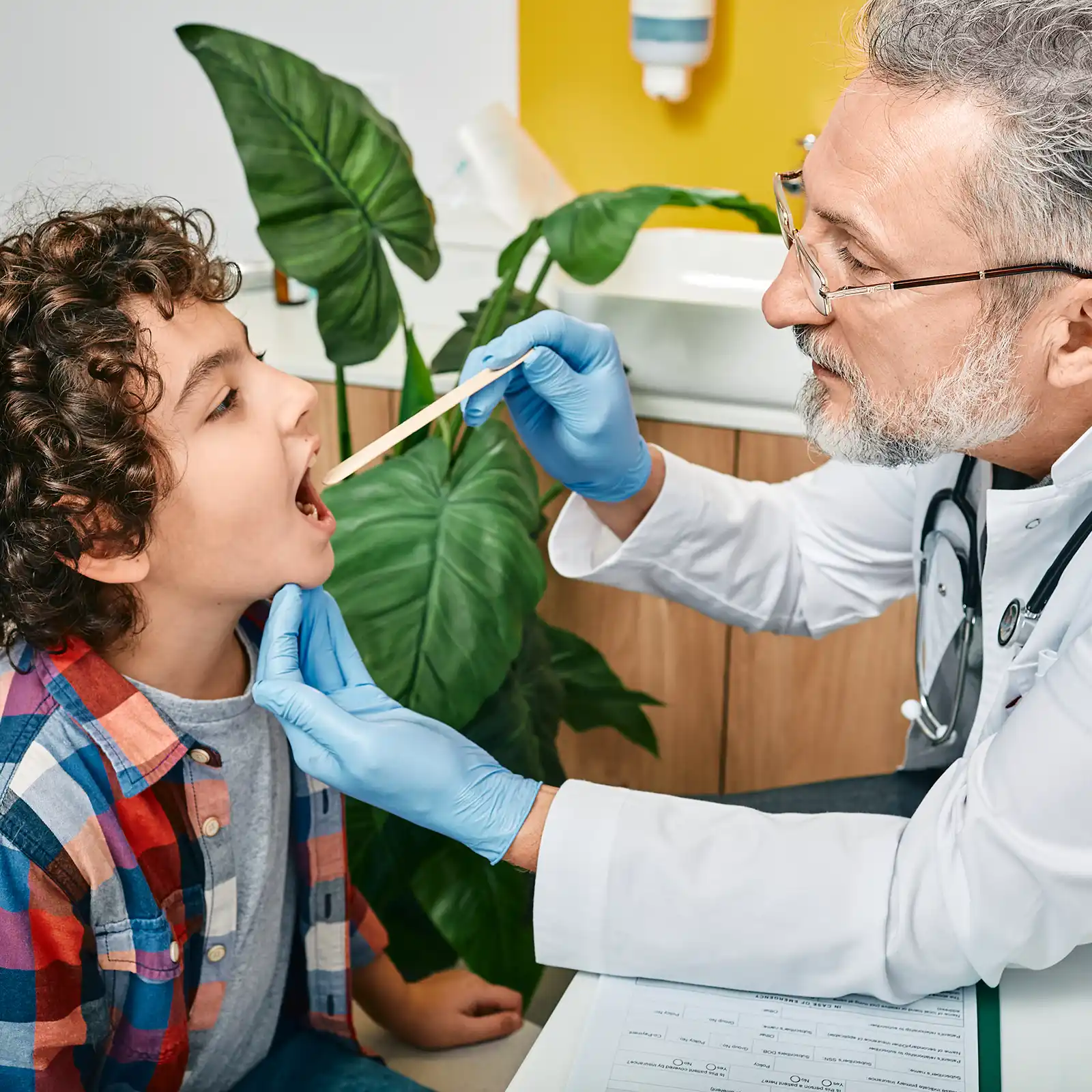 Ein Arzt schaut mithilfe einer Mundspatel in den Hals- und Mundraum eines Kindes. | VIACTIV Krankenkasse