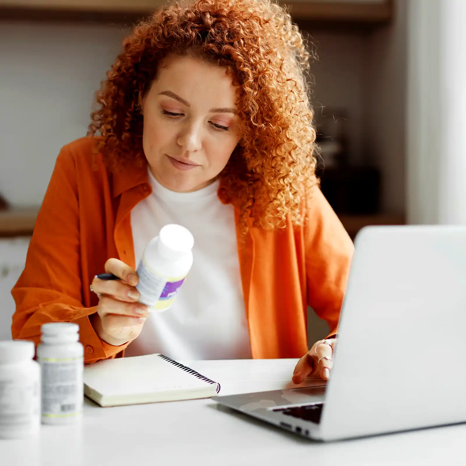 Eine rothaarige Frau liest die Verpackungsrückseite ihrer Supplements. | VIACTIV Krankenkasse