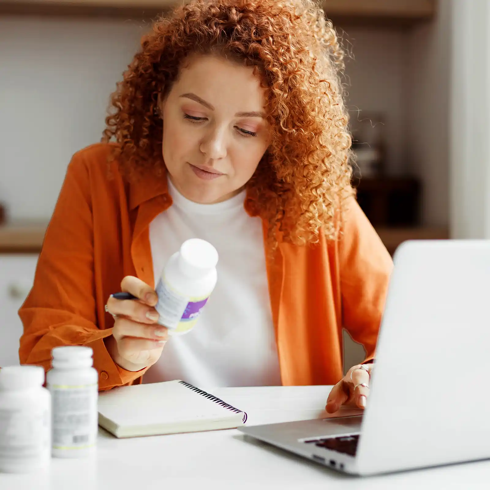 Eine rothaarige Frau liest die Verpackungsrückseite ihrer Supplements. | VIACTIV Krankenkasse