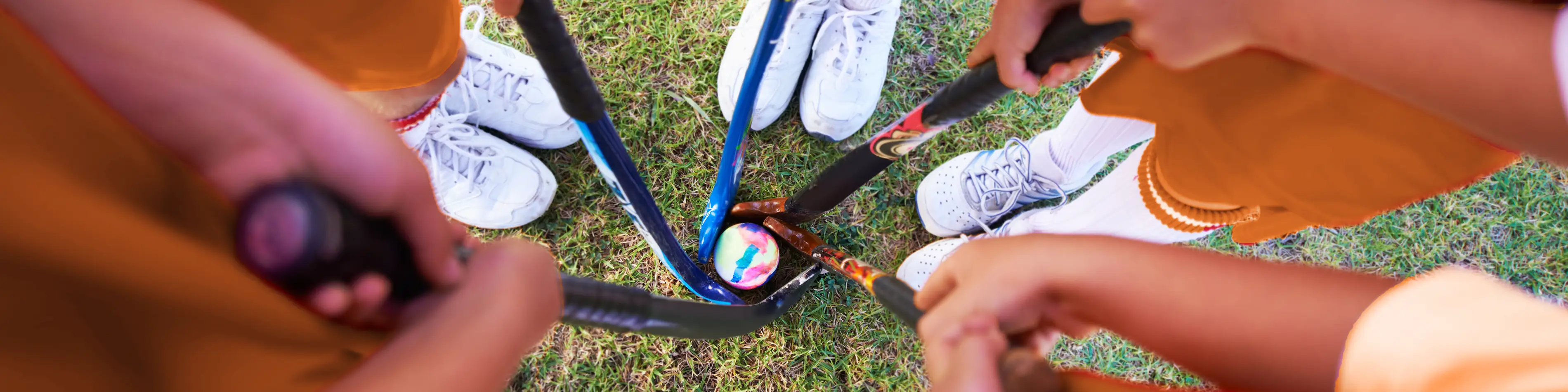 Das Bild zeigt aus Vogelperspektive die Füße einer Gruppe von Sportlern. Sie bilden einen Kreis. In der Mitte liegt ein Hockeyball, der von Hockeyschlägern umkreist wird. | VIACTIV Krankenkasse
