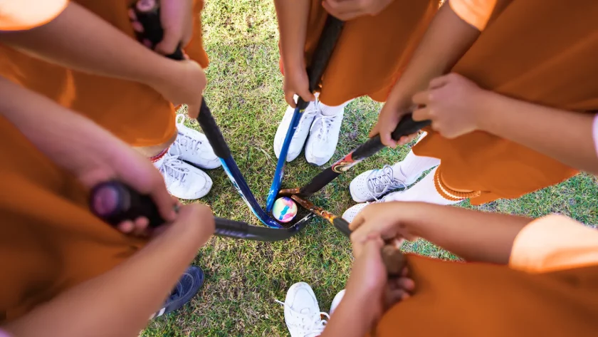Eine Gruppe Sportler hält Hockeyschläger in der Hand. Das Foto ist aus der Vogelperspektive gemacht. Die Gruppe steht im Kreis und in der Mitte liegt ein Hockeball. Dieser wird von Hockeyschlägern umrundet. | VIACTIV Krankenkasse