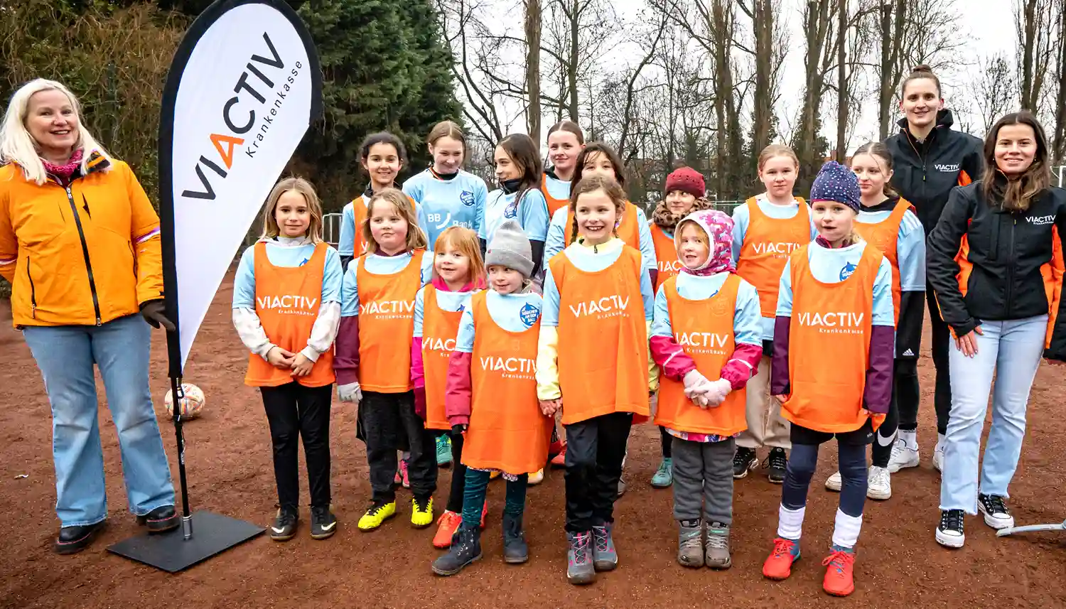 Das Gruppenfoto zeigt eine Gruppe junger Mädchen draußen auf dem Fußballplatz. Bei ihnen stehen die Organisatoren der VIACTIV Krankenkasse, die dieses kostenlose Training für Mädchen anbieten. | VIACTIV Krankenkasse