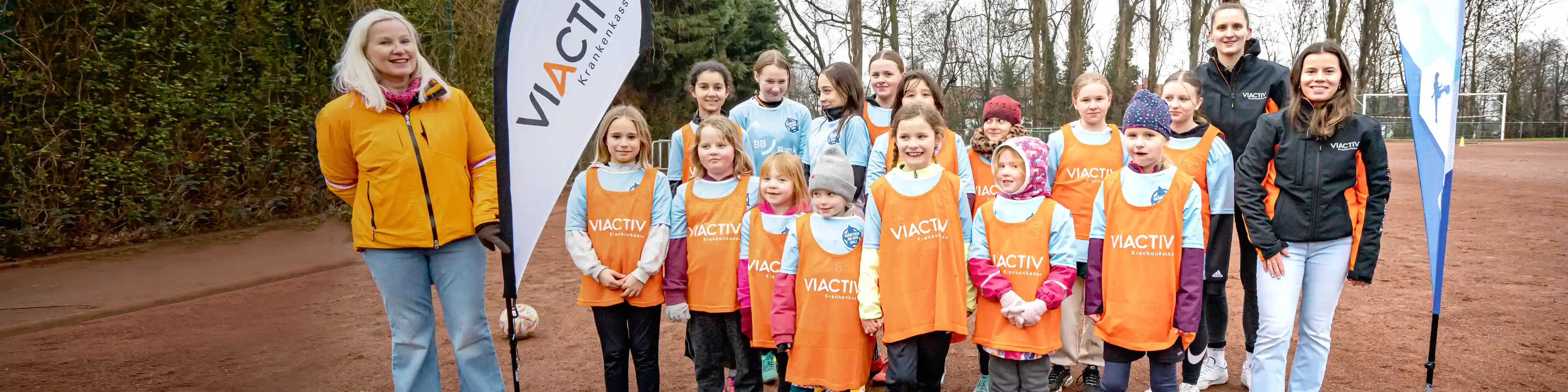 Das Gruppenfoto zeigt eine Gruppe junger Mädchen draußen auf dem Fußballplatz. Bei ihnen stehen die Organisatoren der VIACTIV Krankenkasse, die dieses kostenlose Training für Mädchen anbieten. | VIACTIV Krankenkasse