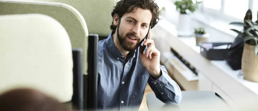 Ein Mann mittleren Alters sitzt im Büro und telefoniert mit seinem Handy. | VIACTIV Krankenkasse