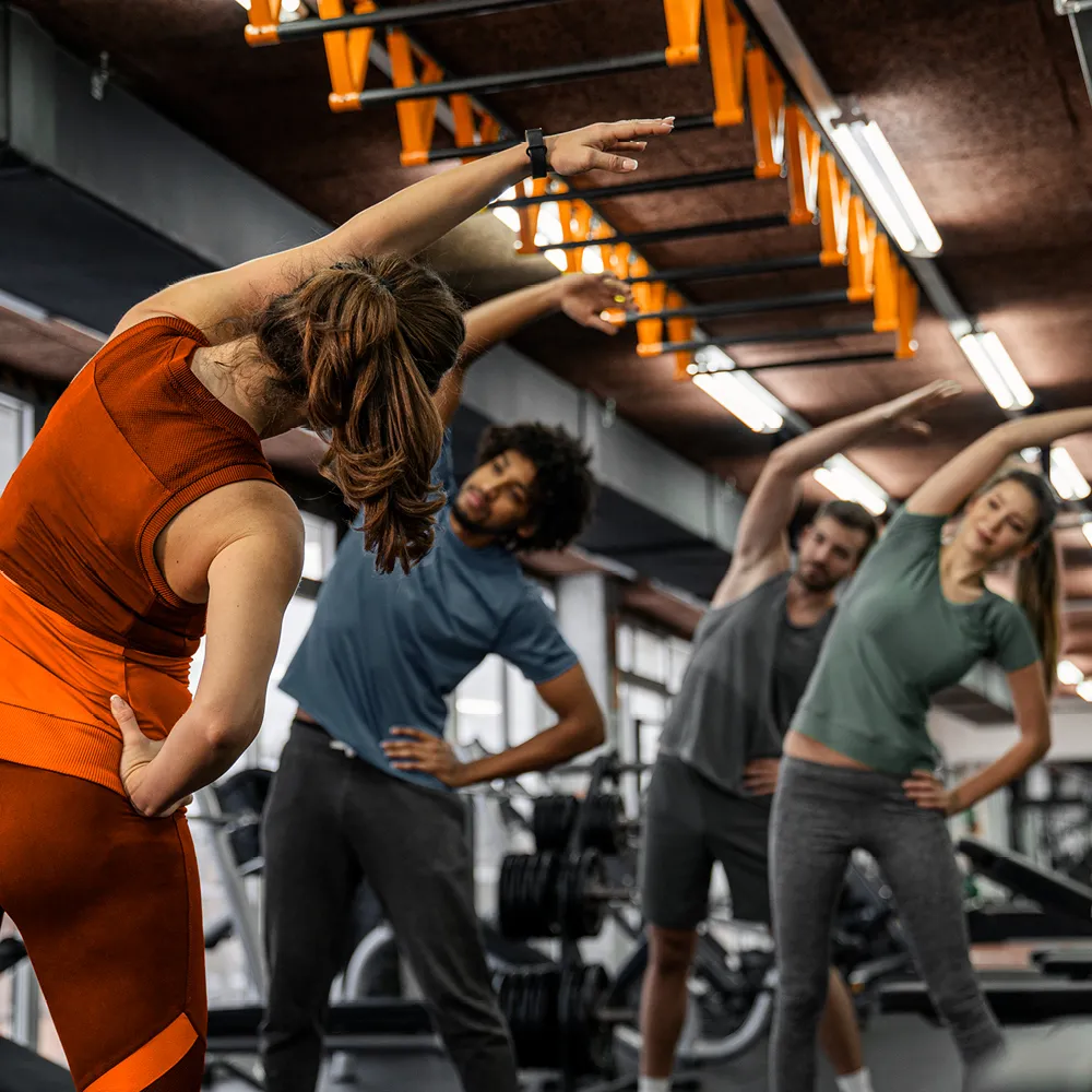 Vier Personen stehen im Fitnessstudio und machen gemeinsam die Übung Seitbeuger. | VIACTIV Krankenkasse