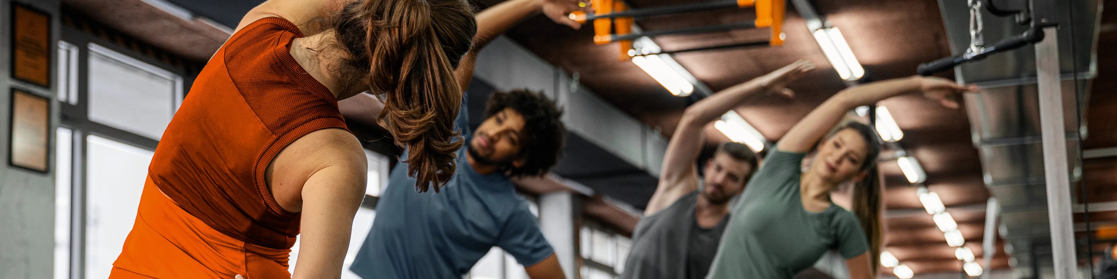 Vier Personen stehen im Fitnessstudio und machen gemeinsam die Übung Seitbeuger. | VIACTIV Krankenkasse