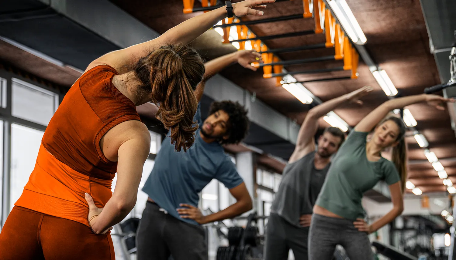 Vier Personen stehen im Fitnessstudio und machen gemeinsam die Übung Seitbeuger. | VIACTIV Krankenkasse