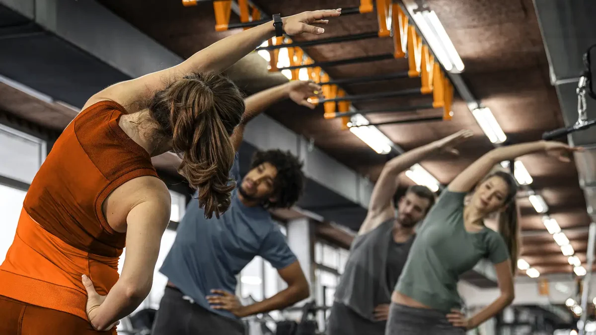 Vier Personen stehen im Fitnessstudio und machen gemeinsam die Übung Seitbeuger. | VIACTIV Krankenkasse