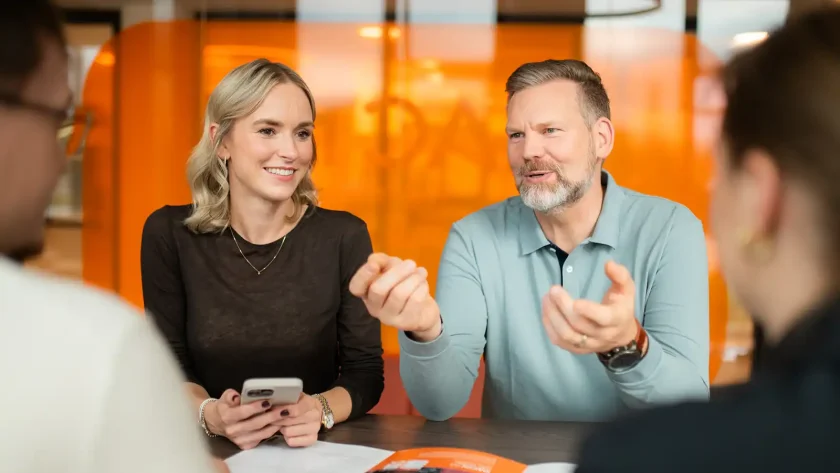 Eine Gruppe von VIACTIV Mitarbeitenden sitzt am Tisch. Sie unterhalten sich. Eine von ihnen hält ein Handy in der Hand. | VIACTIV Krankenkasse