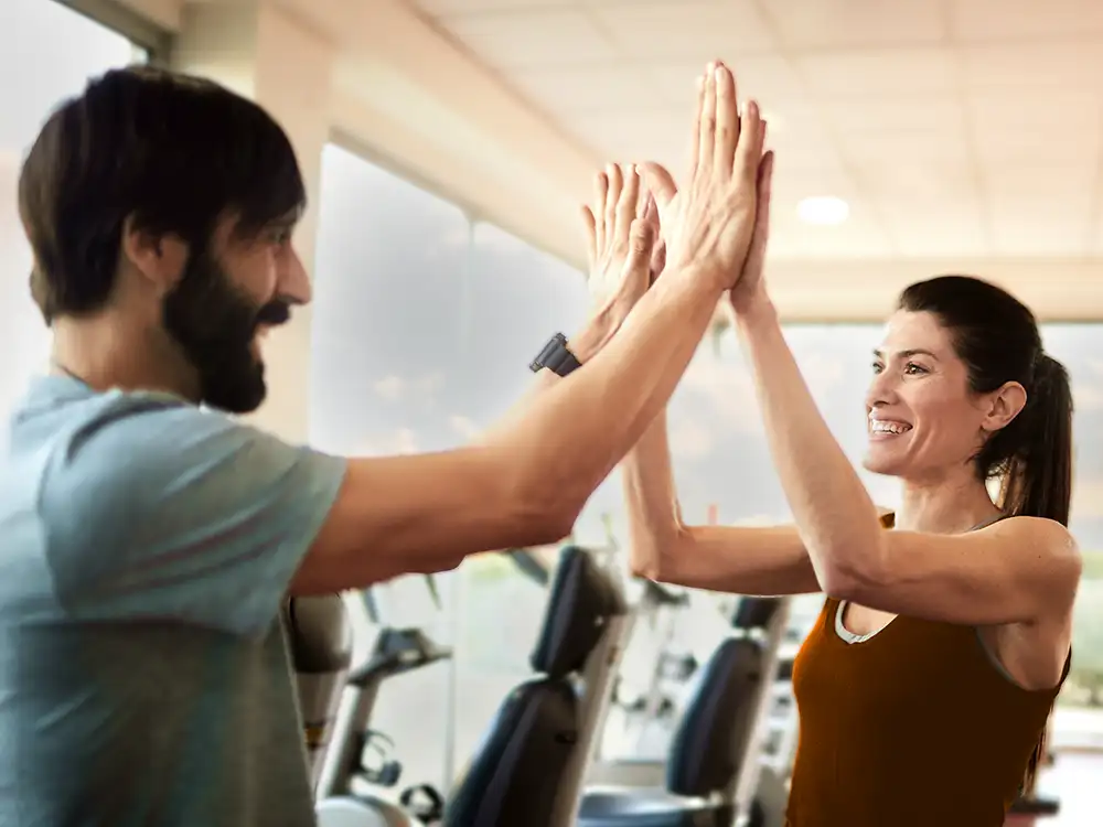 Ein Mann und eine Frau klatschen sich im Fitnessstudio mit den Händen ab. | VIACTIV Krankenkasse