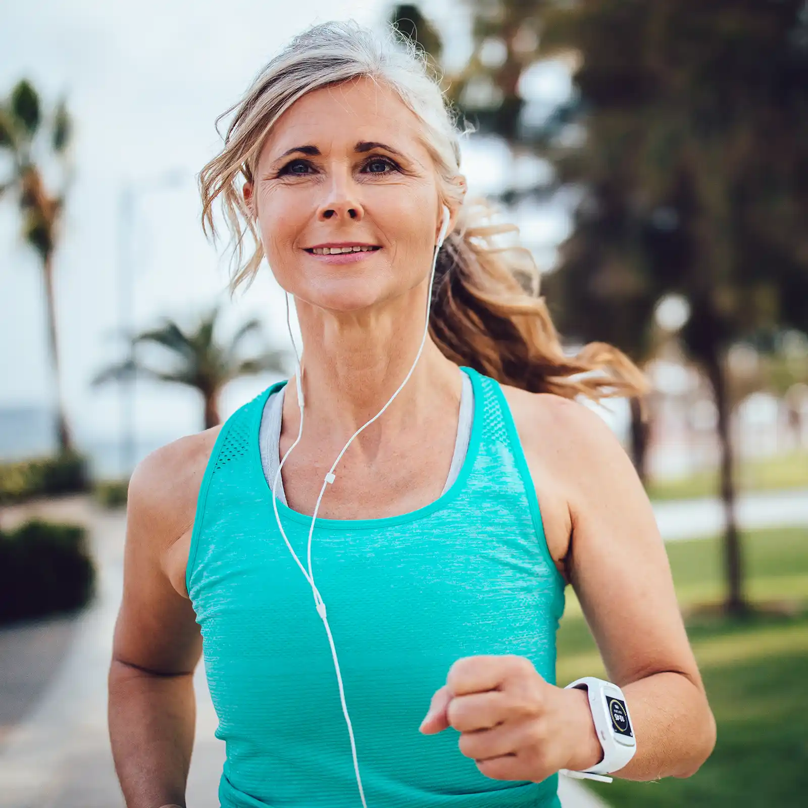 Eine Frau ist zufrieden am Joggen und hört dabei Musik. Im Hintergrund ist eine Wiese mit Bäumen zu sehen. | VIACTIV Krankenkasse