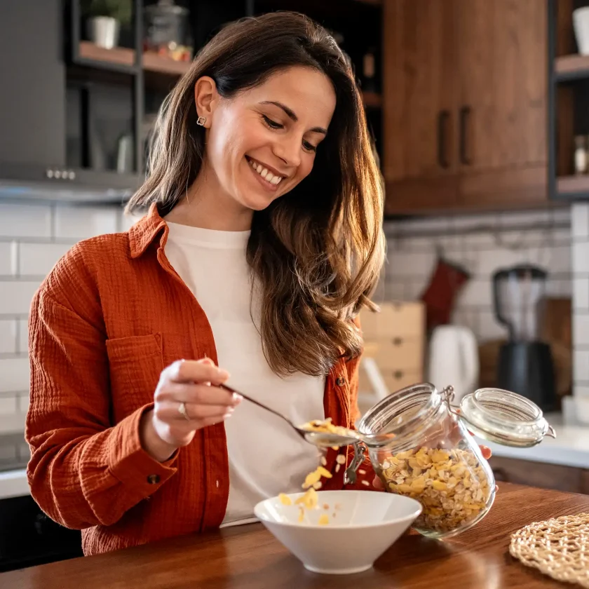 Eine junge Frau steht in der Küche und packt sich gesundes Müsli in eine Schüssel. | VIACTIV Krankenkasse