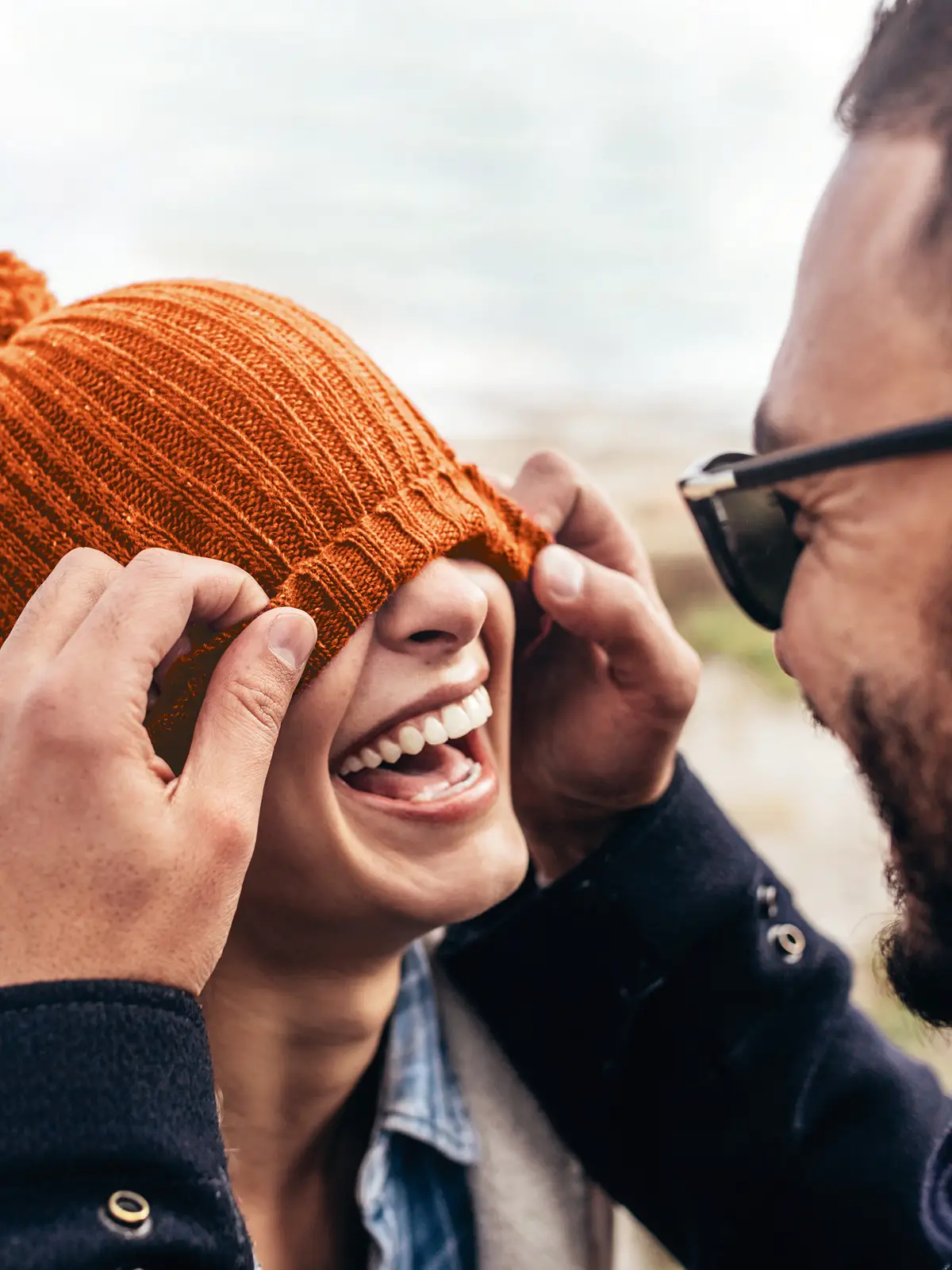 Eine Frau und ein Mann stehen sich gegenüber. Beide lachen und die Frau hat ihre Mütze über die Augen gezogen. | VIACTIV Krankenkasse