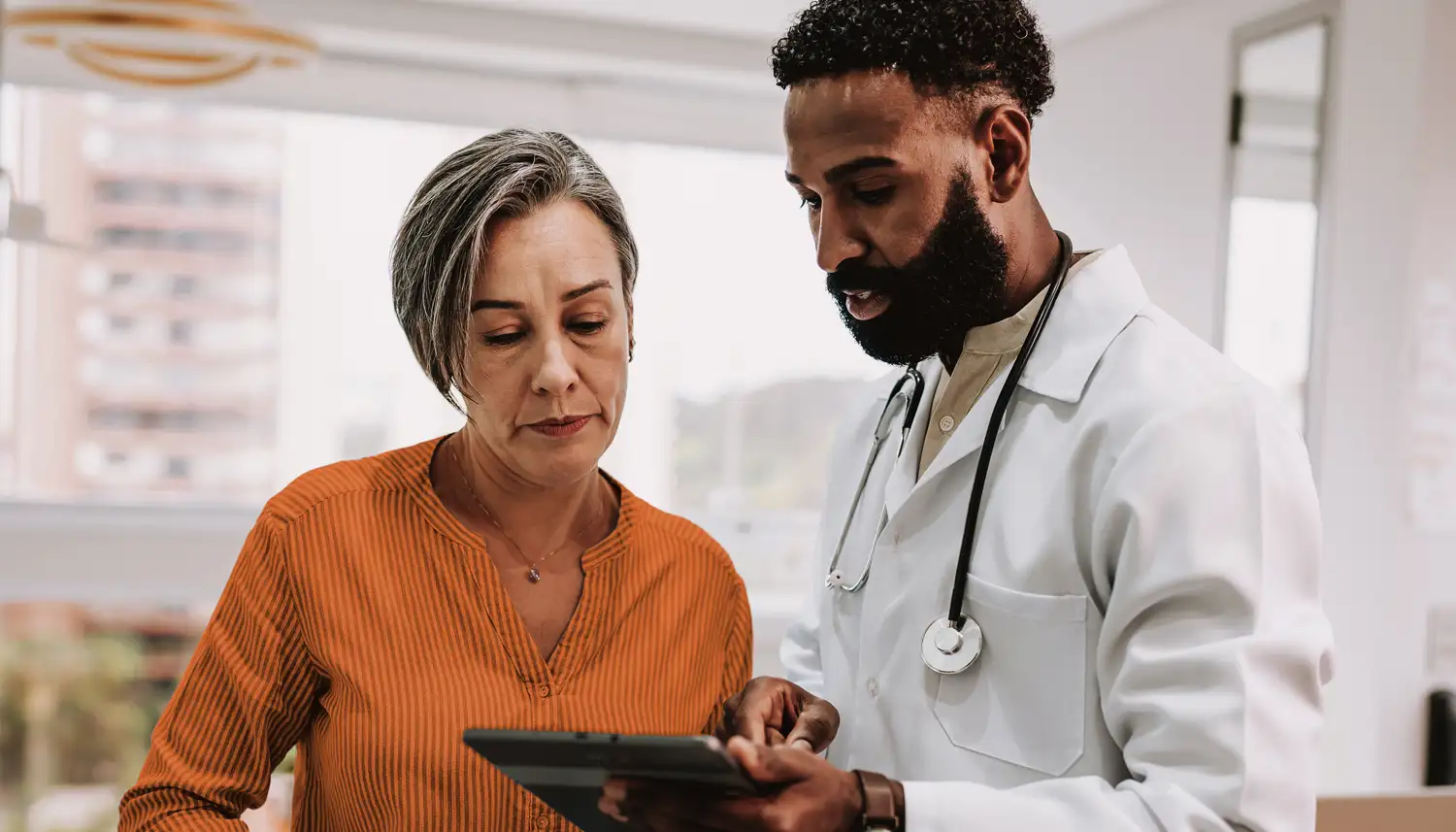 Eine Frau wird von einem Arzt beraten. Beide schauen auf ein Tablet. | VIACTIV Krankenkasse