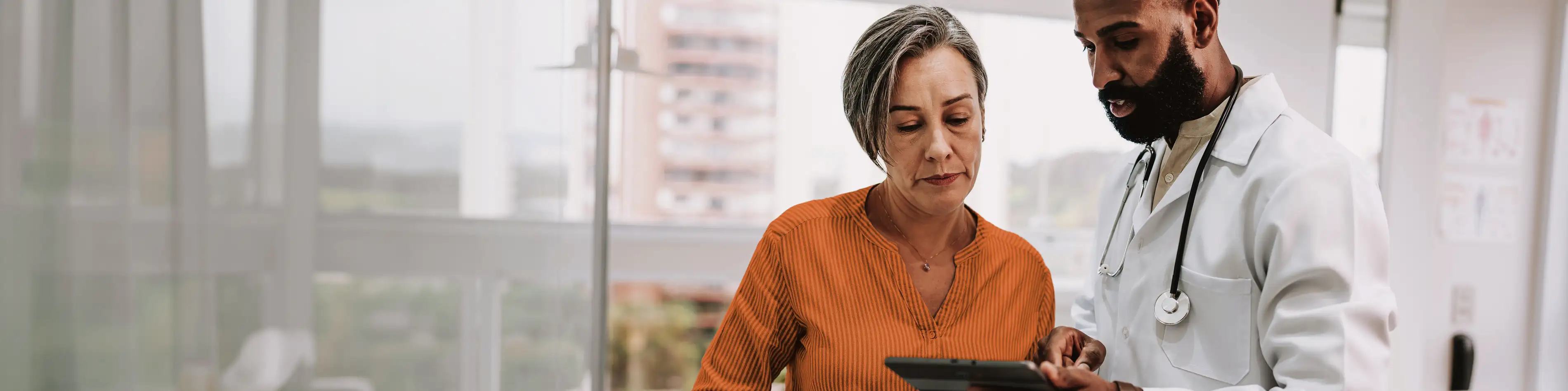 Eine Frau wird von einem Arzt beraten. Beide schauen auf ein Tablet. | VIACTIV Krankenkasse