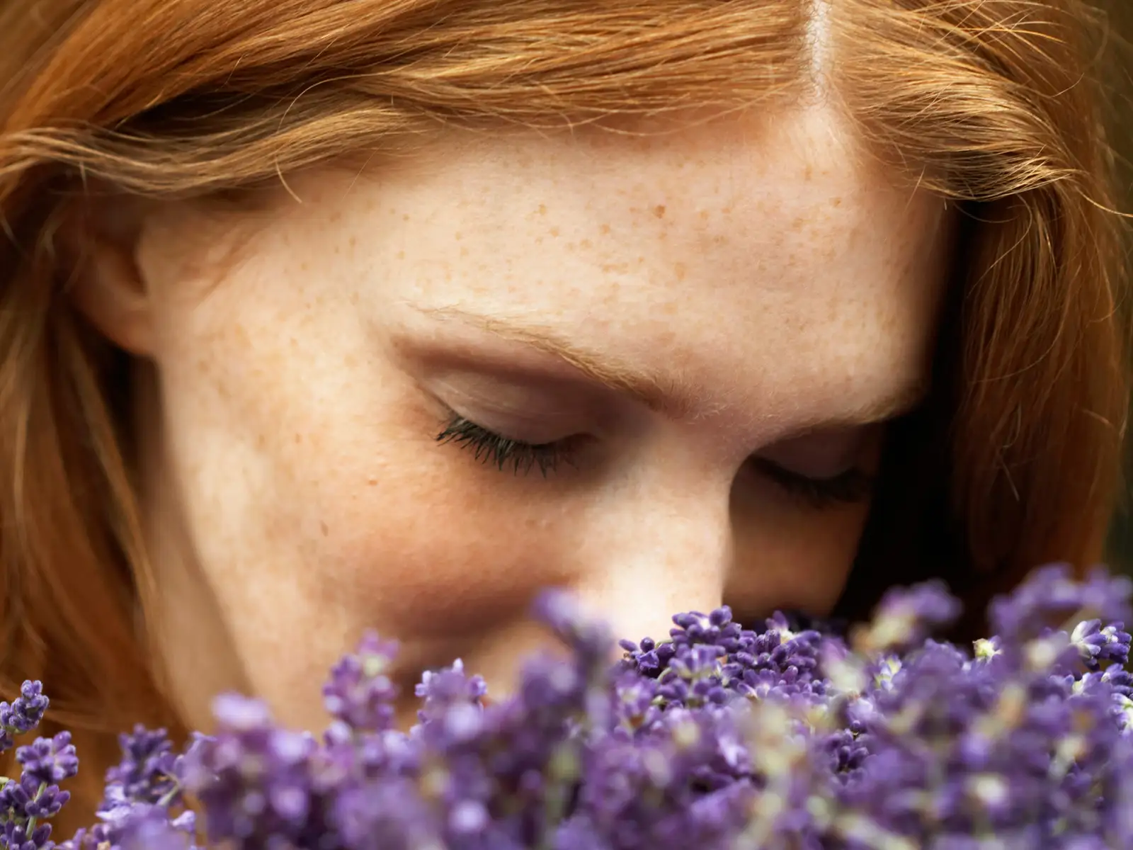 Eine Frau mit rötlichen Haaren riecht an einem Strauß Lavendel und hat die Augen geschlossen. | VIACTIV Krankenkasse