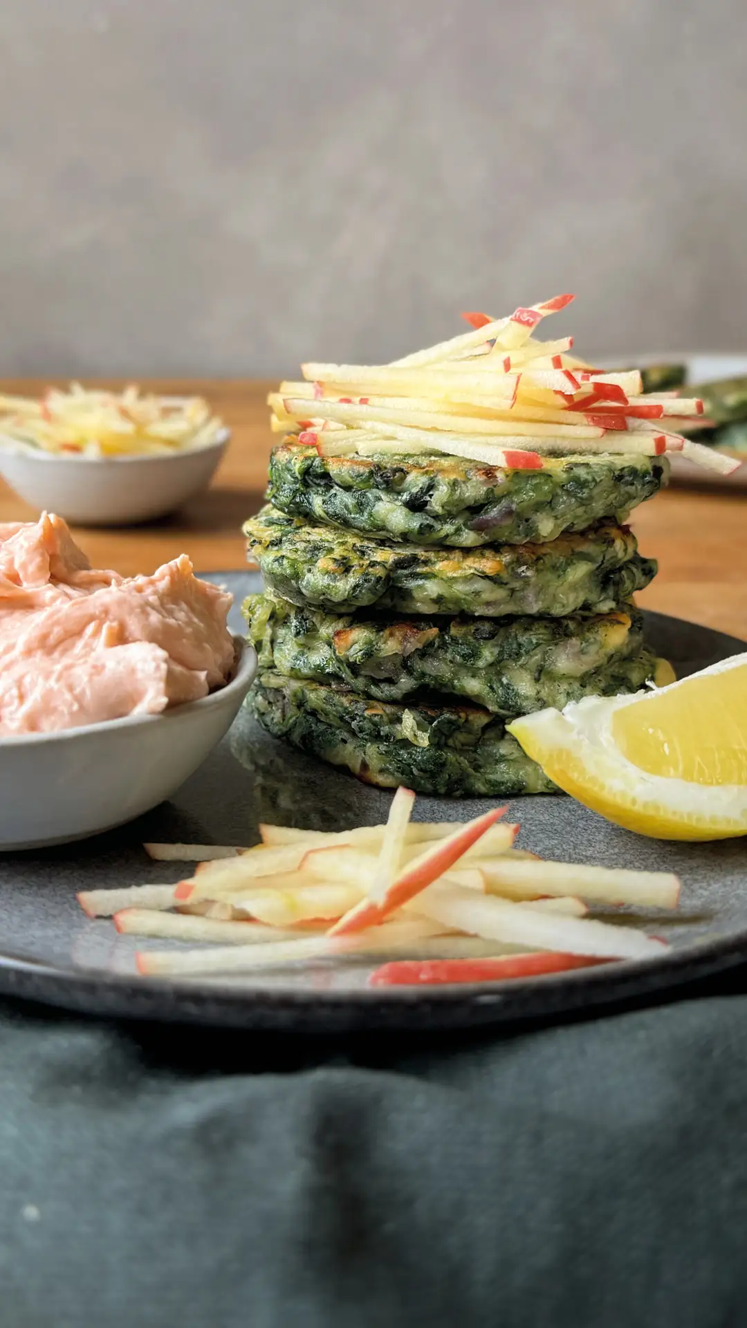 Spinatpuffer garniert mit Apfelstreifen und Zitrone auf einem dunkelgrauen Teller. | VIACTIV Krankenkasse